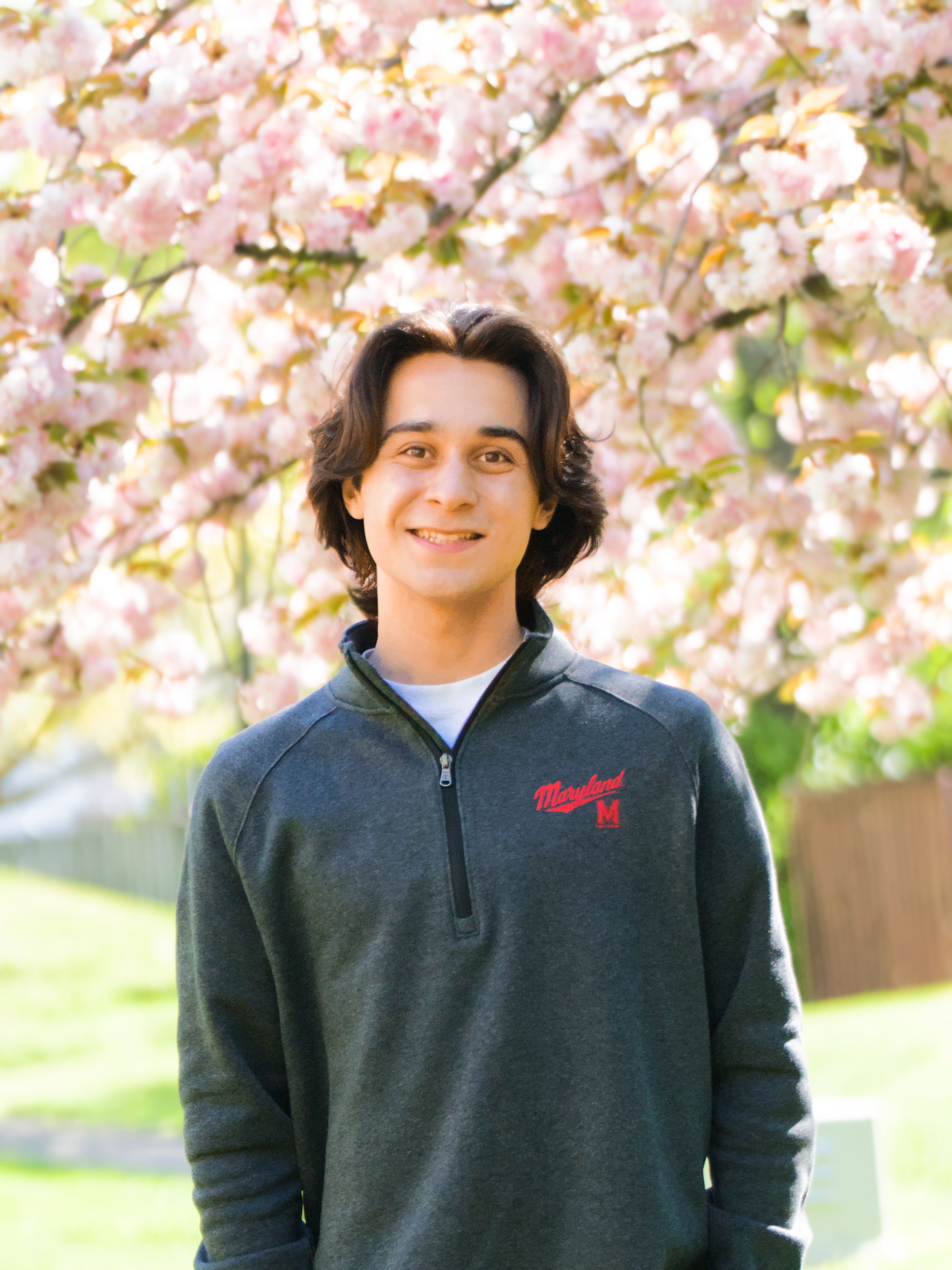 Ben Ross beneath spring blossoms wearing a University of Maryland pullover